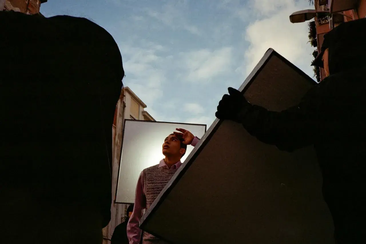 Crew member looking up at a mirror reflector on a street shoot in Lisbon