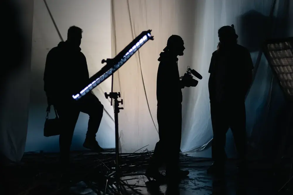 Silhouettes of a film crew with a camera and an LED tube light on set